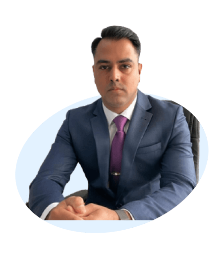 Professional man in a blue suit with a pink tie, sitting with his hands clasped on a desk, against a white background.