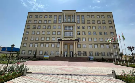 A large, symmetrical six-story building housing TajHind Edutech Pvt Ltd, with a central entrance featuring a balcony and columns. The pathway leading to it is adorned with a patterned design,