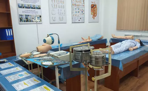 A TajHind Edutech Pvt Ltd medical training room with anatomical models and medical equipment, including dummies on beds, surgical tools on a tray, and educational posters on the walls.